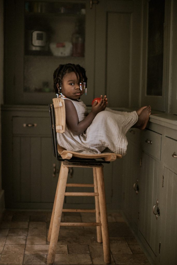 Little girl playing with apple in green pantry during West Michigan in-home lifestyle session with Alissa Saylor
