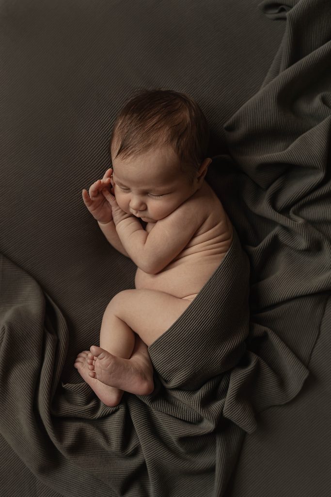 Baby loosely swaddled in dark green blankets for in-home newborn session with Alissa Saylor