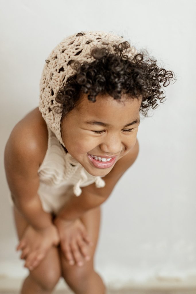 biracial little girl in studio. curly hair bonnet and knit romper