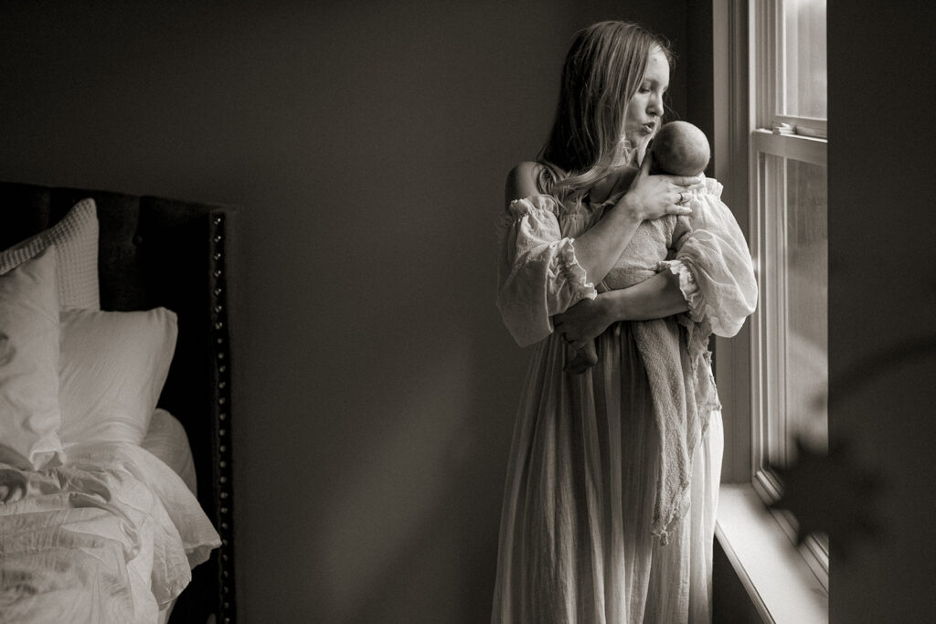 Mom and newborn baby standing in window light in bedroom during newborn session with Alissa Saylor Photography