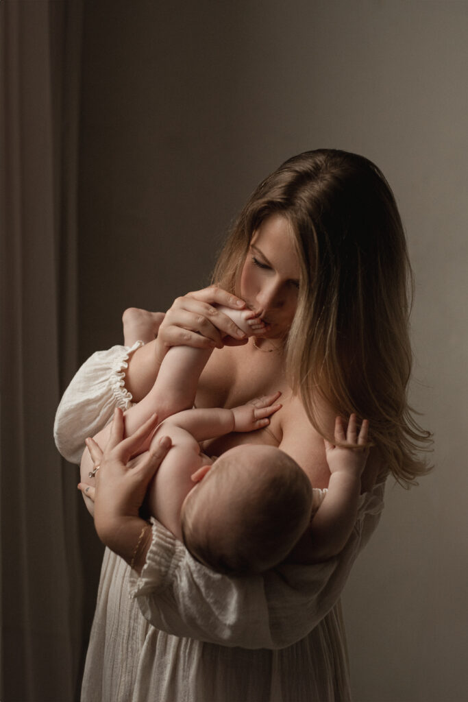 mom kissing toddler toes wearing cream dress during studio session in West Michigan